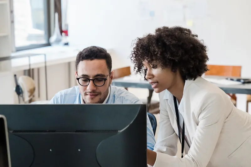 Two colleagues talking through work at a computer.