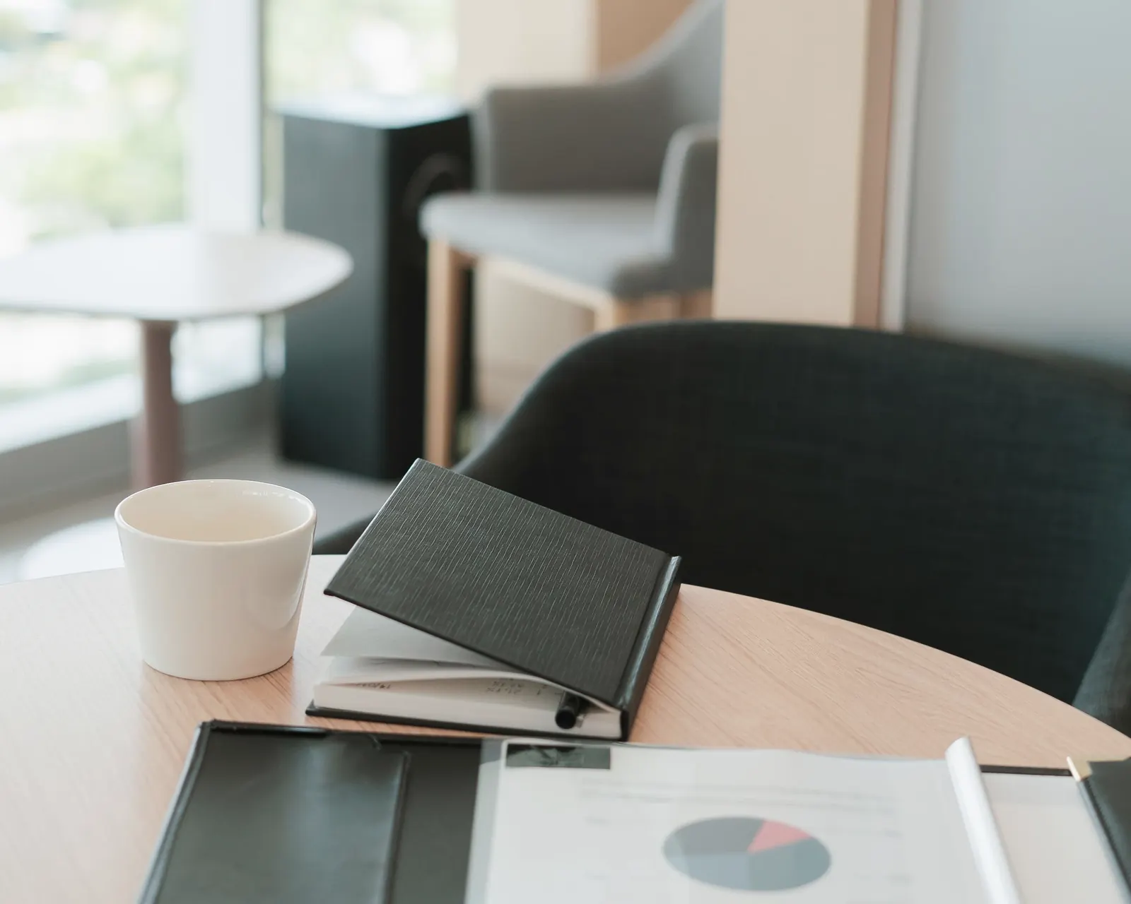 A small table by a window, set with a cup, a notebook and a folder.