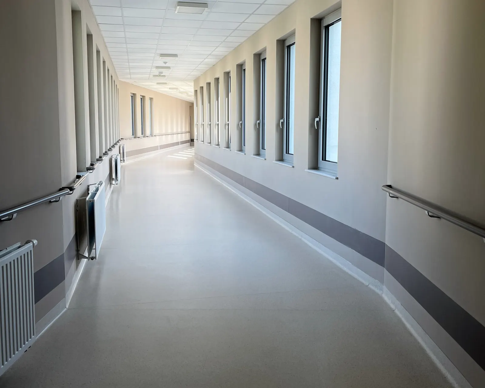 A long hospital corridor in daylight, handrails along both walls.