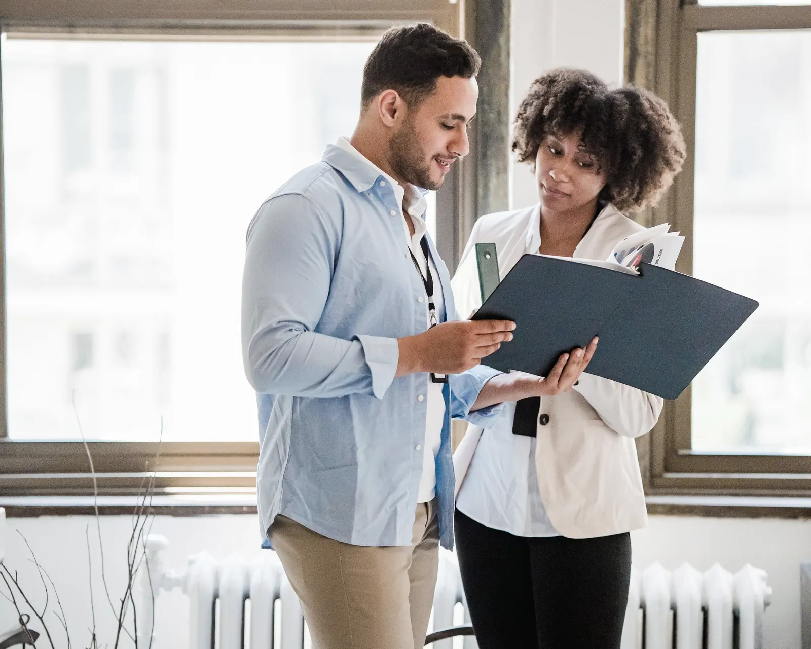 Two colleagues standing by a window, going through a folder together.